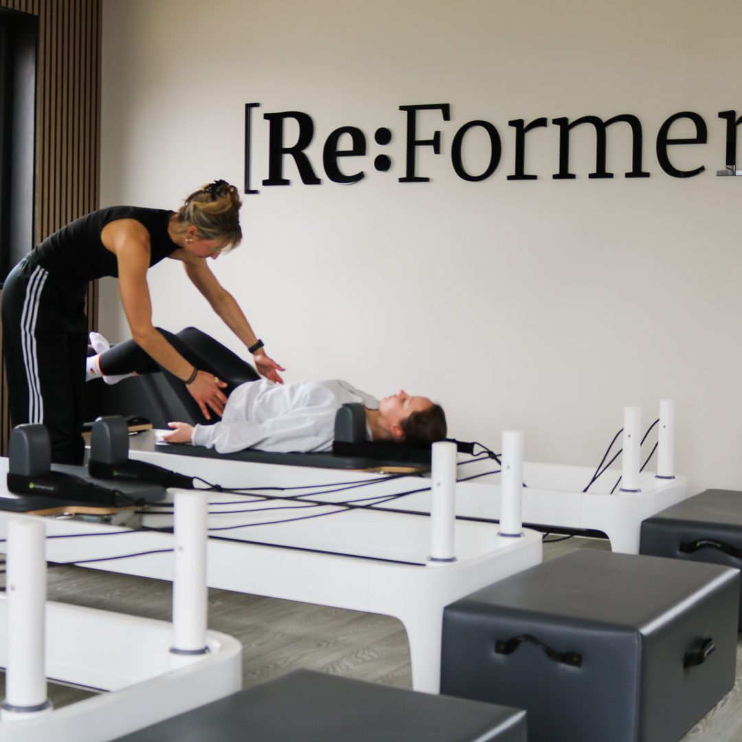 Instructor assisting a participant on a reformer Pilates machine
